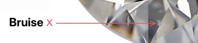 Bruise Inclusion on the Crown Facet of a Diamond Close-up of a diamond showing a visible bruise inclusion on the crown facet, marked with an arrow.